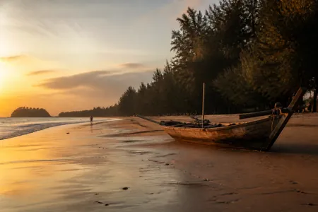 Pantai Cahaya Bulan waktu senja: perahu kayu berlabuh di pasir basah dan pokok ru di tepi pantai